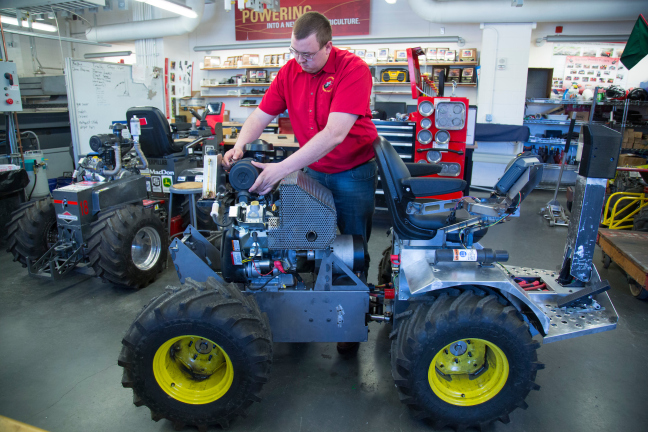 An ISU student works on a new quarter scall tractor inside a workshop
