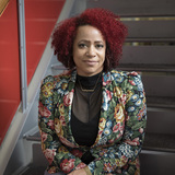 Nikole Hannah-Jones sits on a staircase and looks at the camera with her hands folded in her lap.