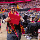 Smiling student holding degree while walking down aisle at Hilton Coliseum during commencement