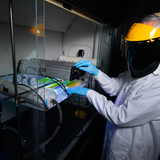 Scientist wearing an ultraviolet face shield works on laboratory equipment and ultraviolet lamps.