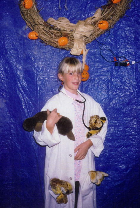 Jessica Ward at six years old dressed as a veterinarian for a Halloween party. She wears a white lab coat and stethoscope and carries stuffed animals.