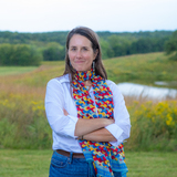 Lisa Schulte Moore standing in front of a farm field featuring native strips of prairie plants