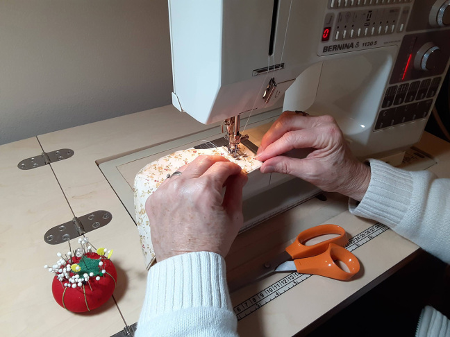 A crafter uses a sewing machine to stitch a cloth face mask.