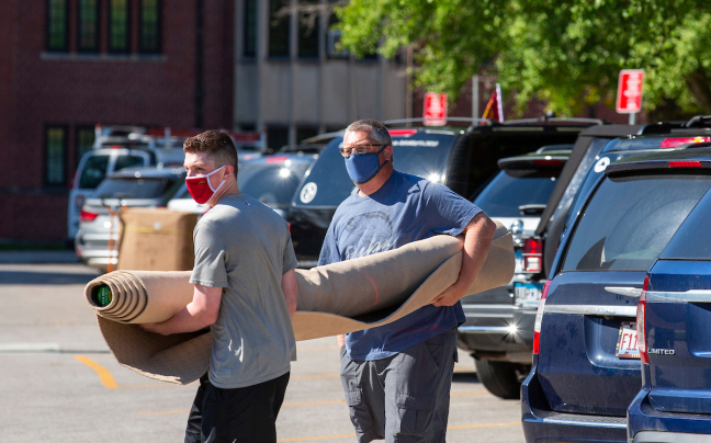 Two people carry a rolled up rug across a parking lot outside Friley Hall at Iowa State University, August 3, 2020.