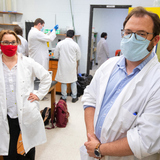 Karin Allenspach and Jon Mochel wear masks and stand in a laboratory while researchers work on lab equipment in the background
