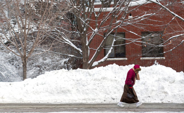 A woman walks past piles of snow on the ISU campus in February 2019.