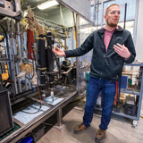 A scientist stands in front of pyrolysis machinery