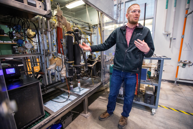 A scientist stands in front of pyrolysis machinery