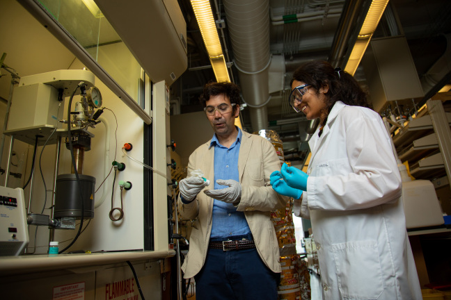 Aaron Sadow and Kajol Tonk standing in a laboratory looking at a small bottle