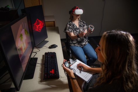 Psychology grad student Taylor Doty, background, uses a VR set, while Maddie Friedman, a senior in psychology, measures her user experience. (Christopher Gannon/Iowa State University)