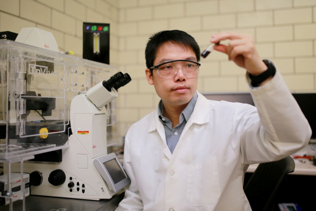 Shan Jiang looking at a vial in lab