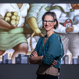 Miriam Martincic smiles and stands in front of one of her illustrations projected onto a wall