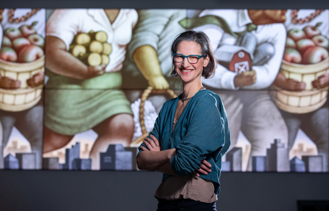 Miriam Martincic smiles and stands in front of one of her illustrations projected onto a wall
