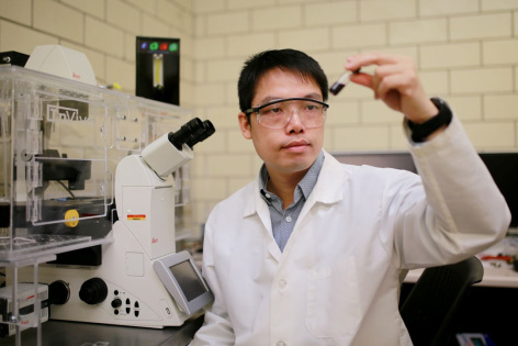 Shan Jiang in a lab holding a small vial with a dark liquid