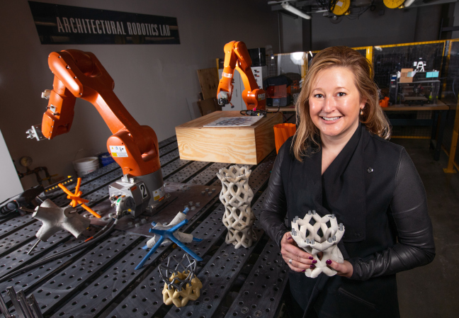 Shelby Doyle stands in front of two robotic arms in a laboratory in the ISU Student Innovation Center