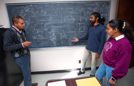 From left, Dr. Rana Parshad, with graduate students Aniket Banerjee and Urvashi Verma, with on formulas on the chalkboard of his Carver Hall office. Photo by Christopher Gannon/Iowa State University.