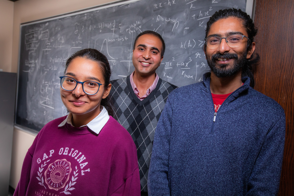 From left, graduate student Urvashi Verma, Dr. Rana Parshad, and graduate student Aniket Banerjee, with on formulas on the chalkboard of Parshad’s Carver Hall office. Photo by Christopher Gannon/Iowa State University.