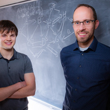 Iowa State senior Addison Schmidt (left) and associate professor of mathematics Claus Kadelka stand in front of a chalk board with depictions of a gene regulatory network in Carver Hall. Photo by Christopher Gannon/Iowa State University.