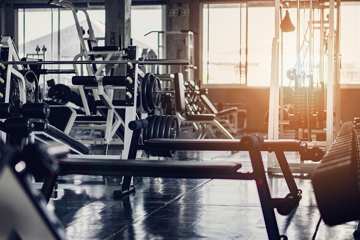 Sunlight streams through a window, lighting up the interior of a room filled with weightlifting machines. Photo credit: Adobe Stock.