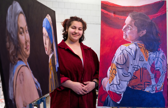 An ISU student stands between two portraits in a studio in the College of Design