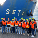 Students wearing safety vests posing in front of a large ship.