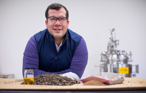Nacu Hernandez wears safety goggles and leans over a table covered with asphalt samples at a laboratory in the ISU Research Park