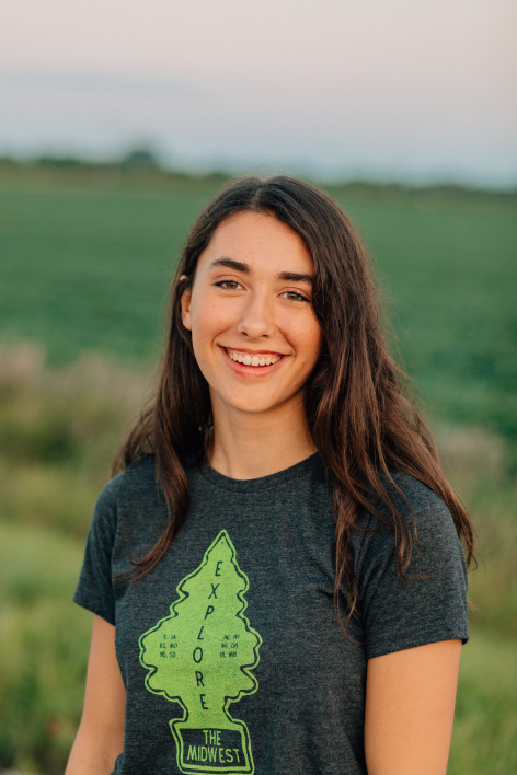 Emma Alstott stands in front of a green agricultural field